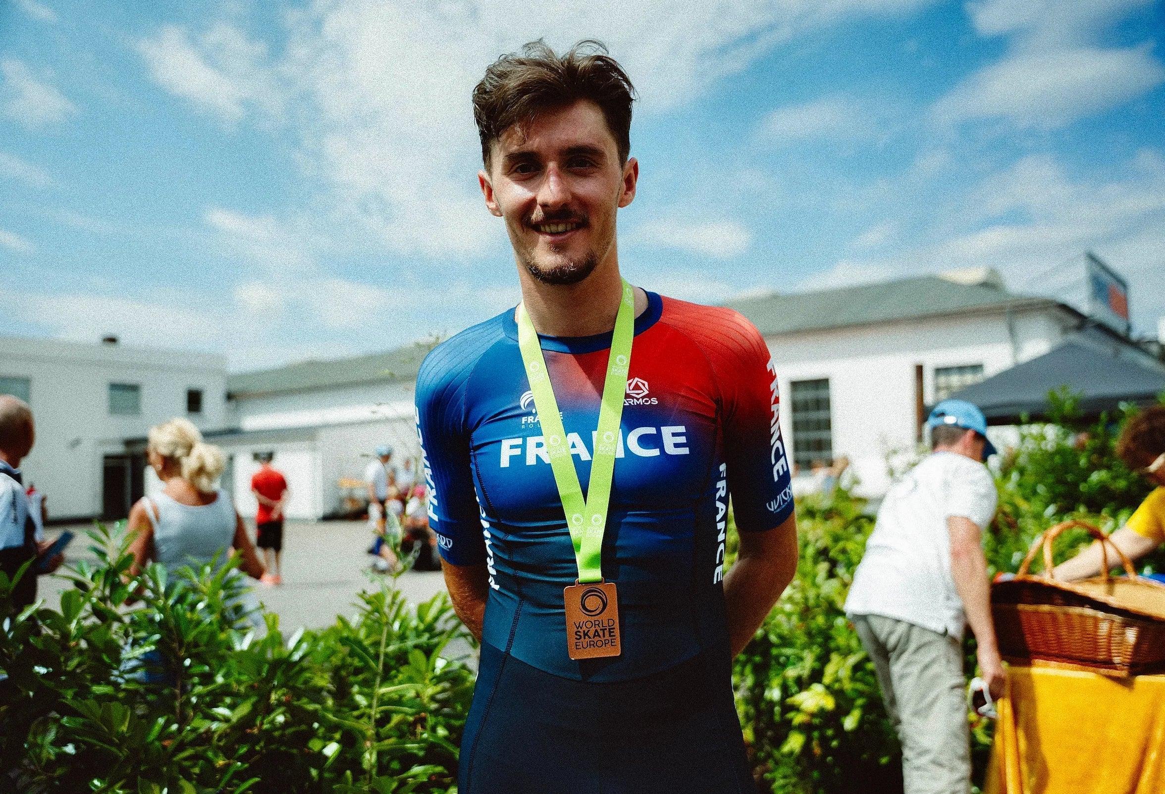 Man in a cycling outfit with 'France' on his jersey, standing outdoors with a blue sky.