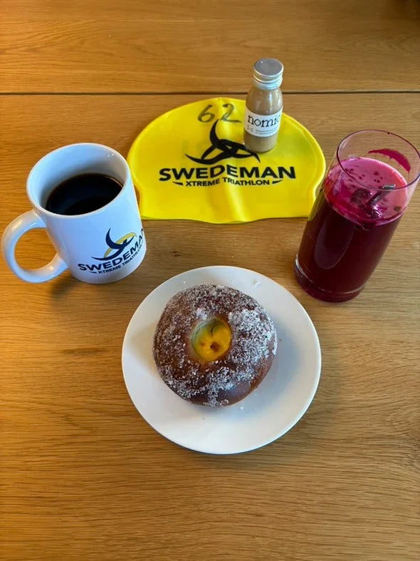 Donut, coffee, beetroot juice stamox, and Swedeman branded items on a wooden table