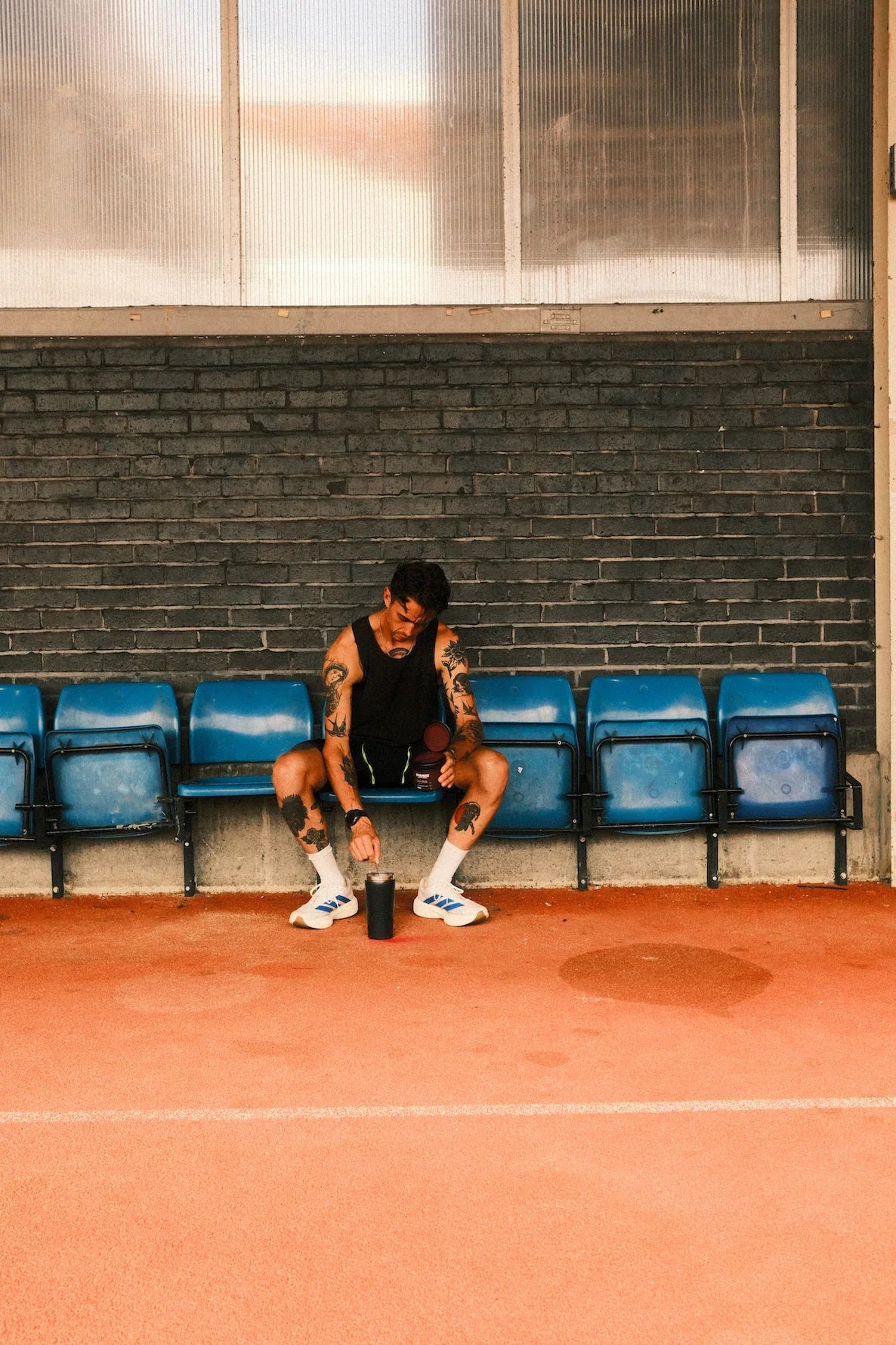 Person sitting on a bench in a track court with a brick wall in the background using stamox beetroot powder