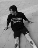 Man in black t-shirt with stamox beetroot powder text, sitting on pavement, promoting endurance