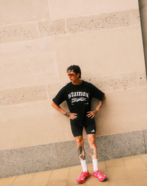 Man in sporty attire posing outdoors, wearing stamox beetroot powder t-shirt and pink sneakers