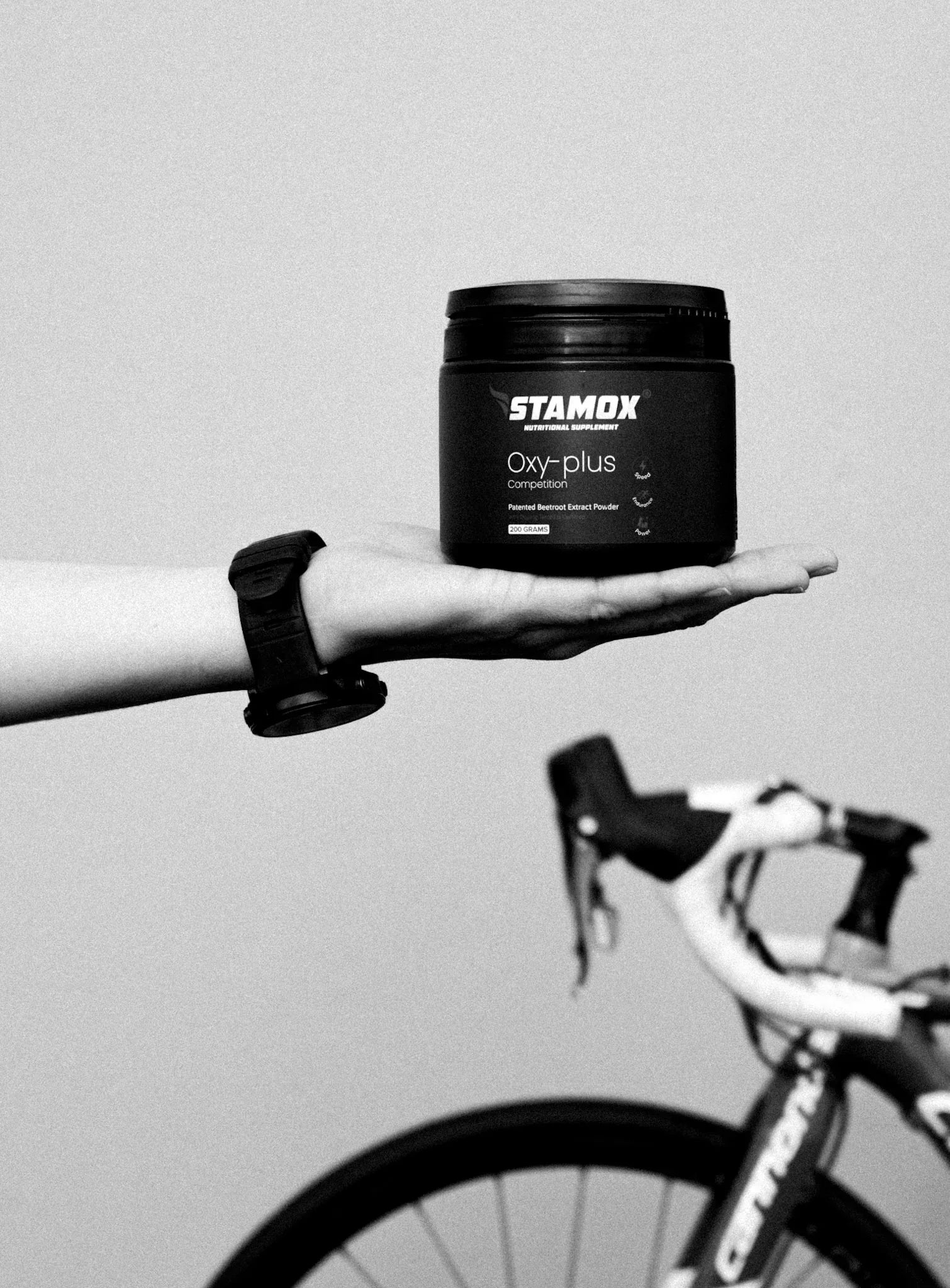Hand holding Stamox beetroot powder with a bicycle in the background, sports supplement