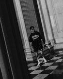 Athletic man in Stamox Beetroot Powder shirt, black shorts, walking on checkered floor