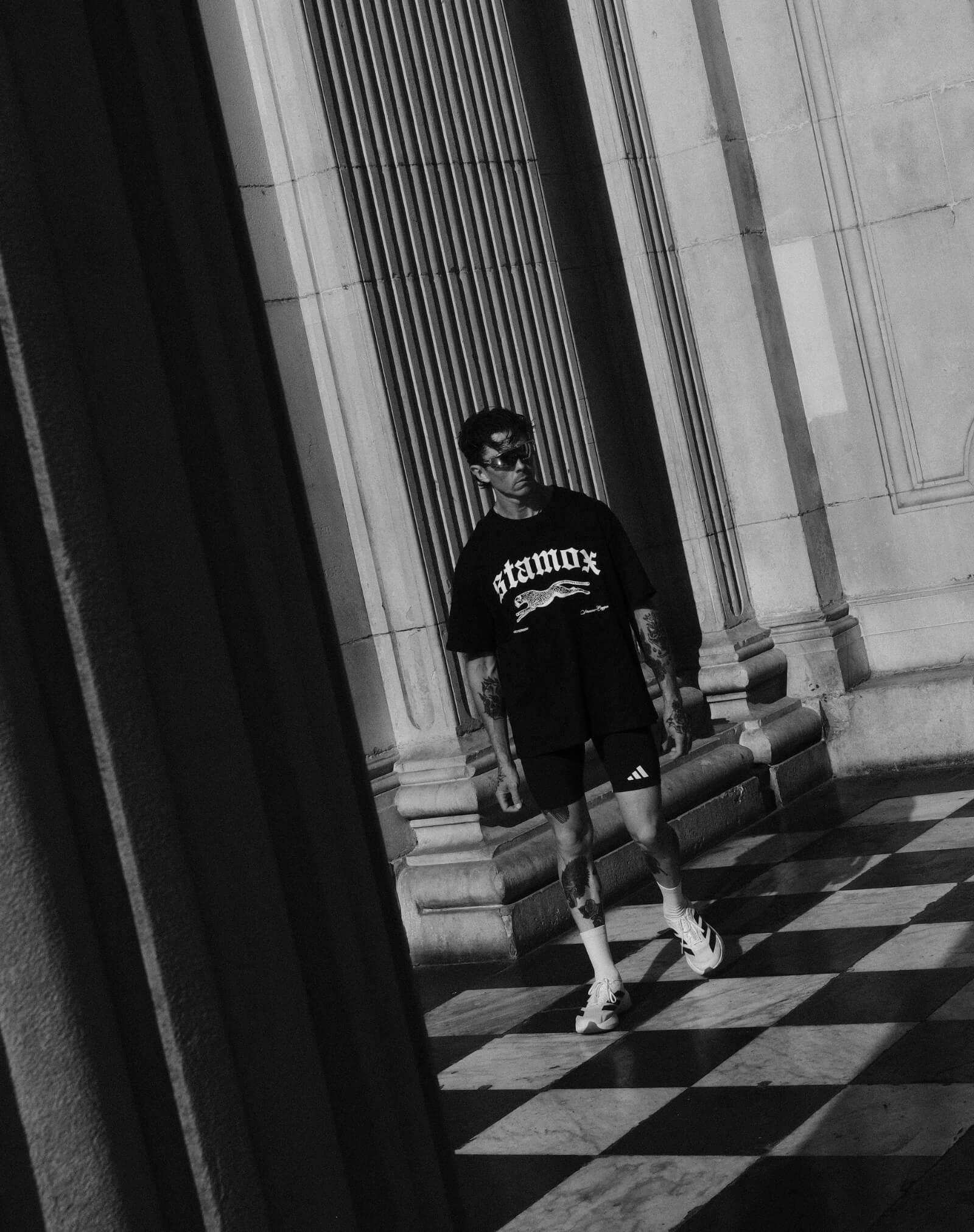 Athletic man in Stamox Beetroot Powder shirt, black shorts, walking on checkered floor