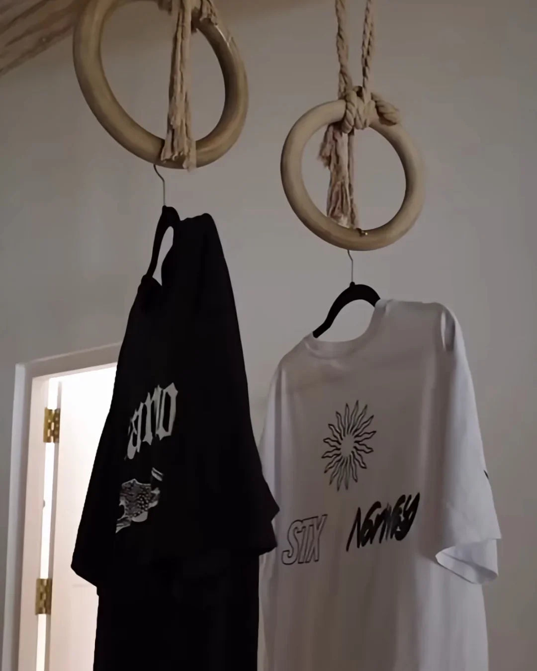 Two graphic t-shirts hanging on gym rings, stamox beetroot powder lifestyle display