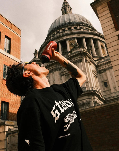 Man outdoors drinking from bottle featuring stamox beetroot powder in urban city setting