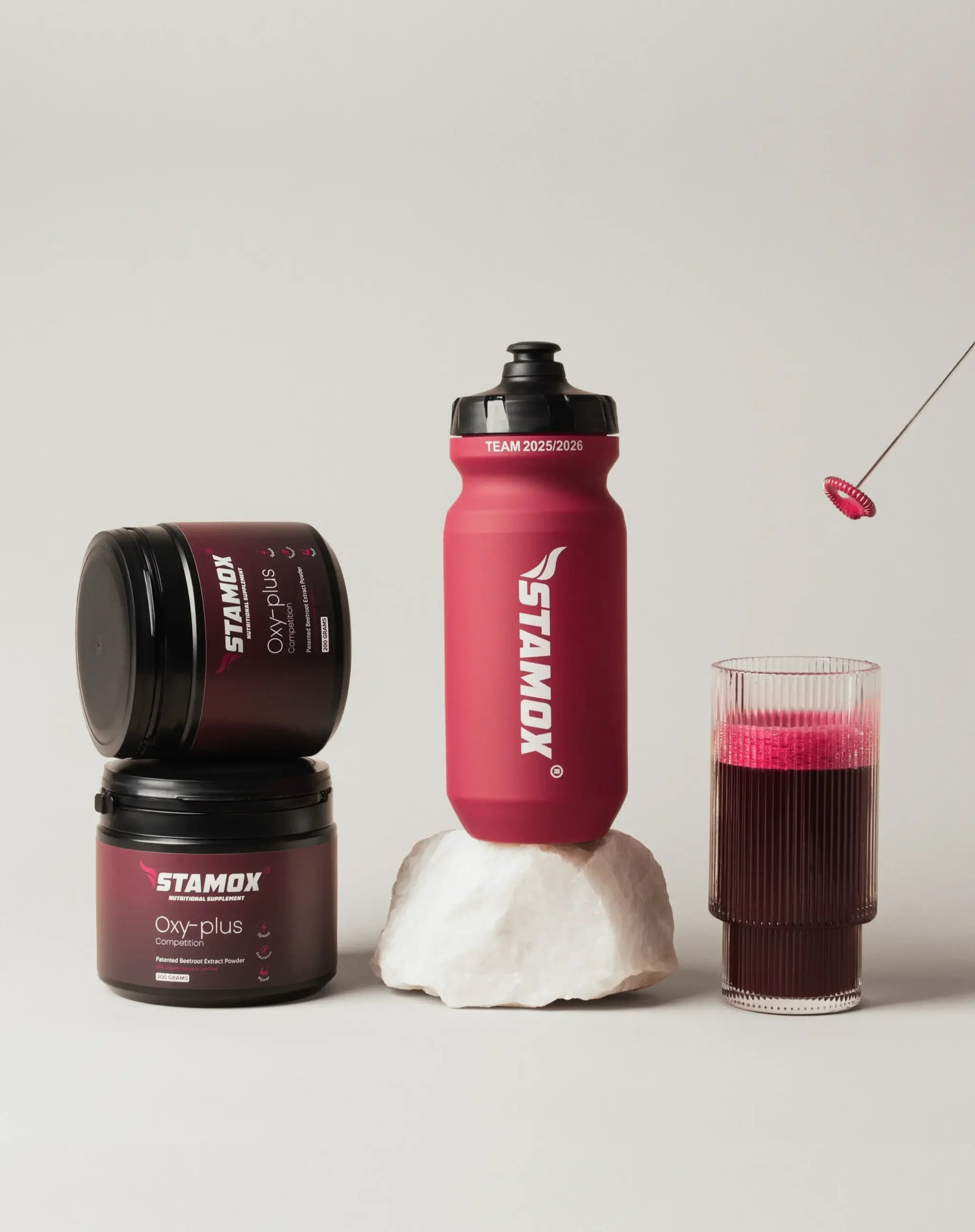 Stamox beetroot powder jars, red water bottle, glass of beetroot drink and whisk on neutral background