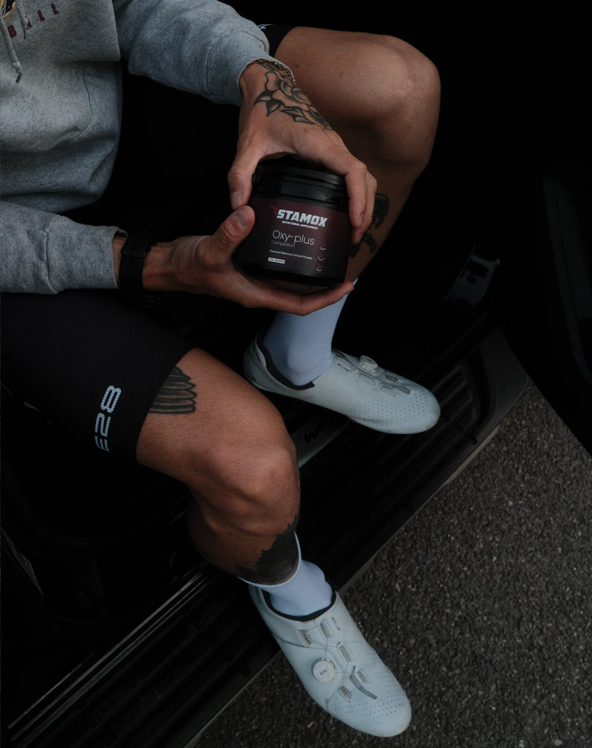 Athlete holding Stamox Oxy-plus beetroot powder supplement, wearing cycling gear and shoes