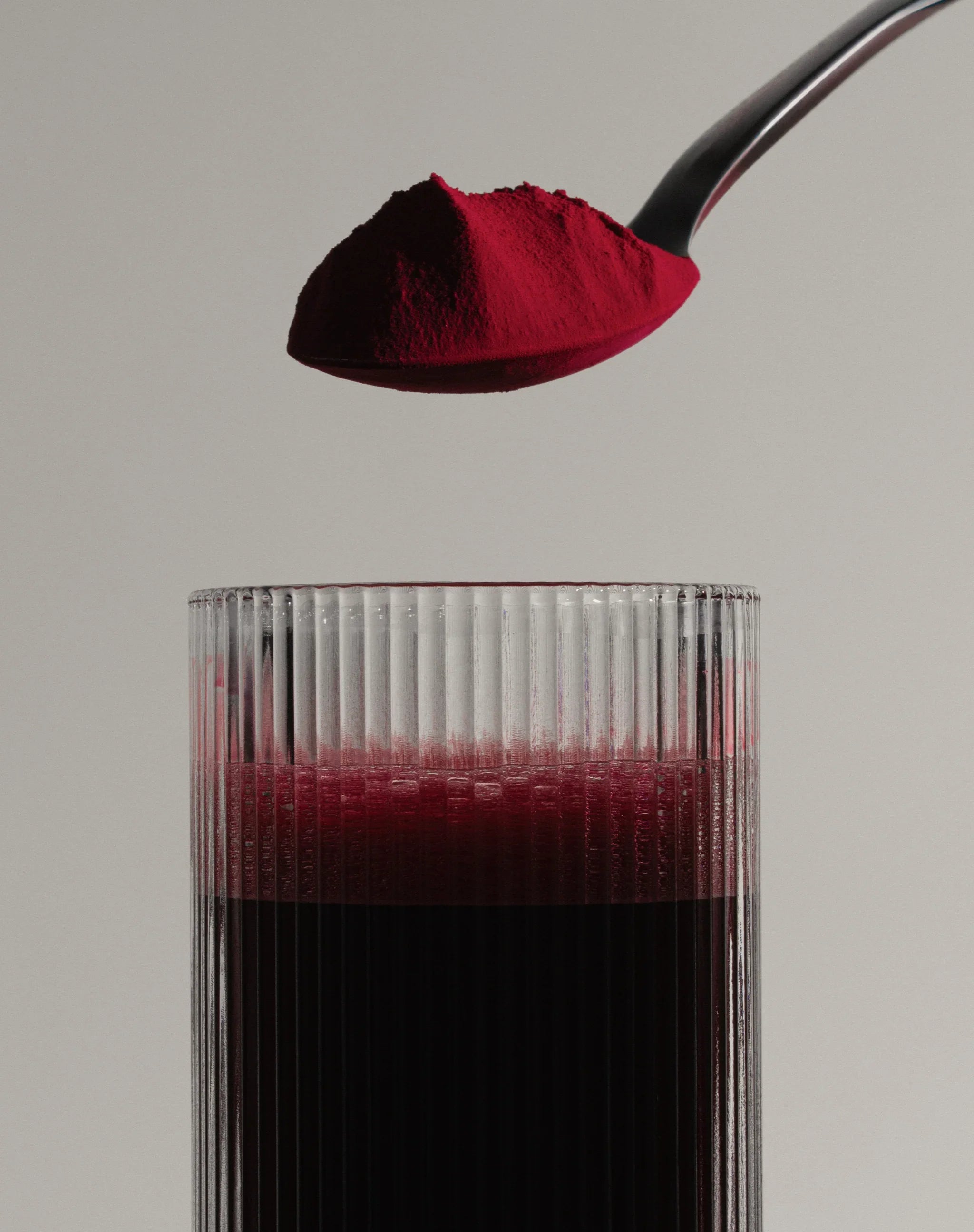 Spoonful of vibrant beetroot powder over a glass of deep red beet juice, boosting endurance and recovery.