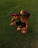 Athlete drinking stamox beetroot powder from red bottle on sports field under sunlight