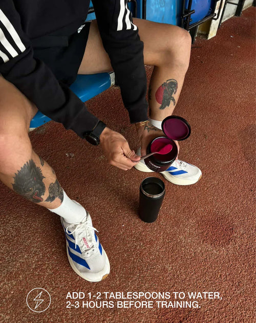 Athlete scooping stamox beetroot powder into a shaker before workout on running track
