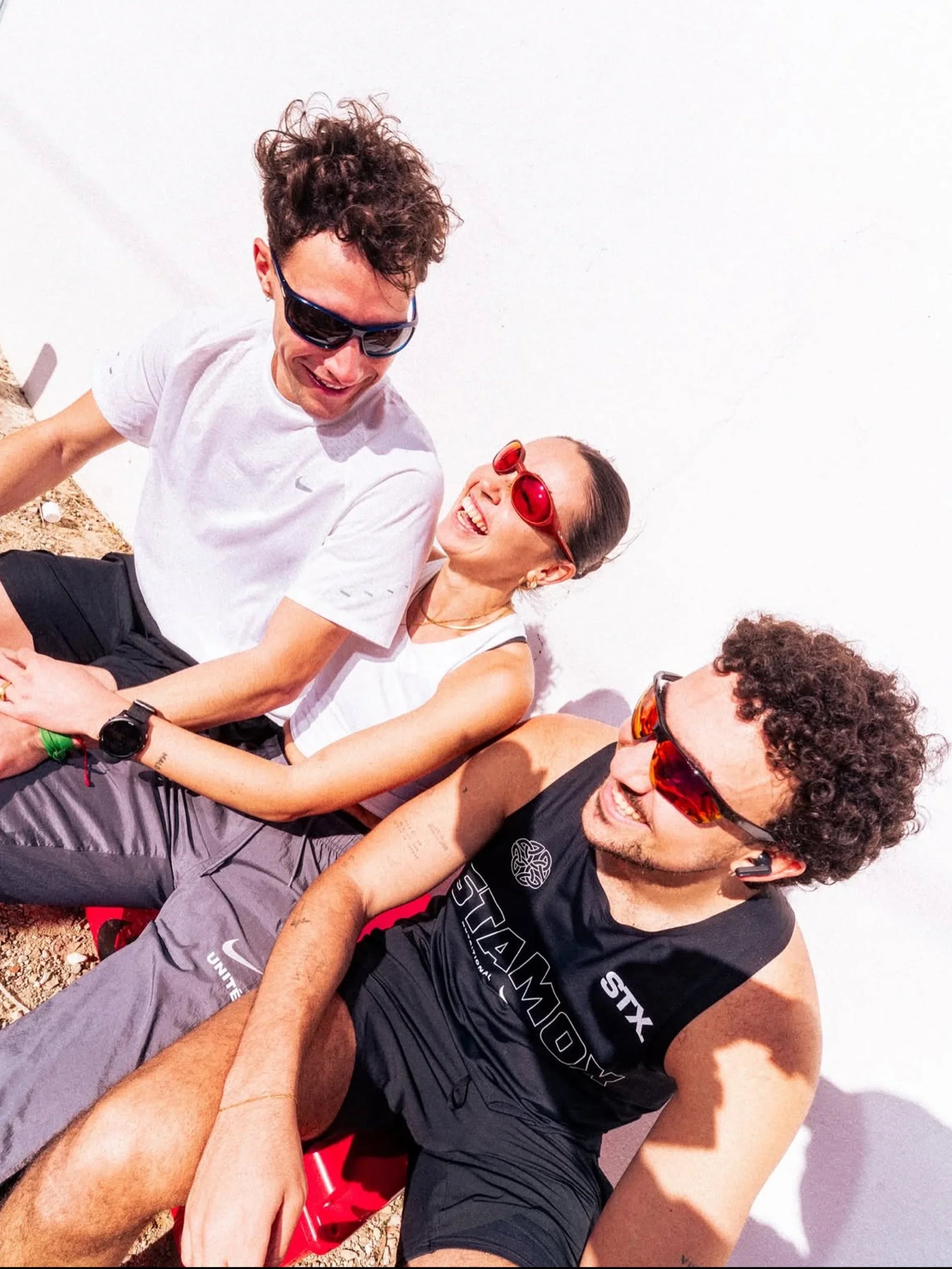 Three people sitting together outdoors, wearing sunglasses.