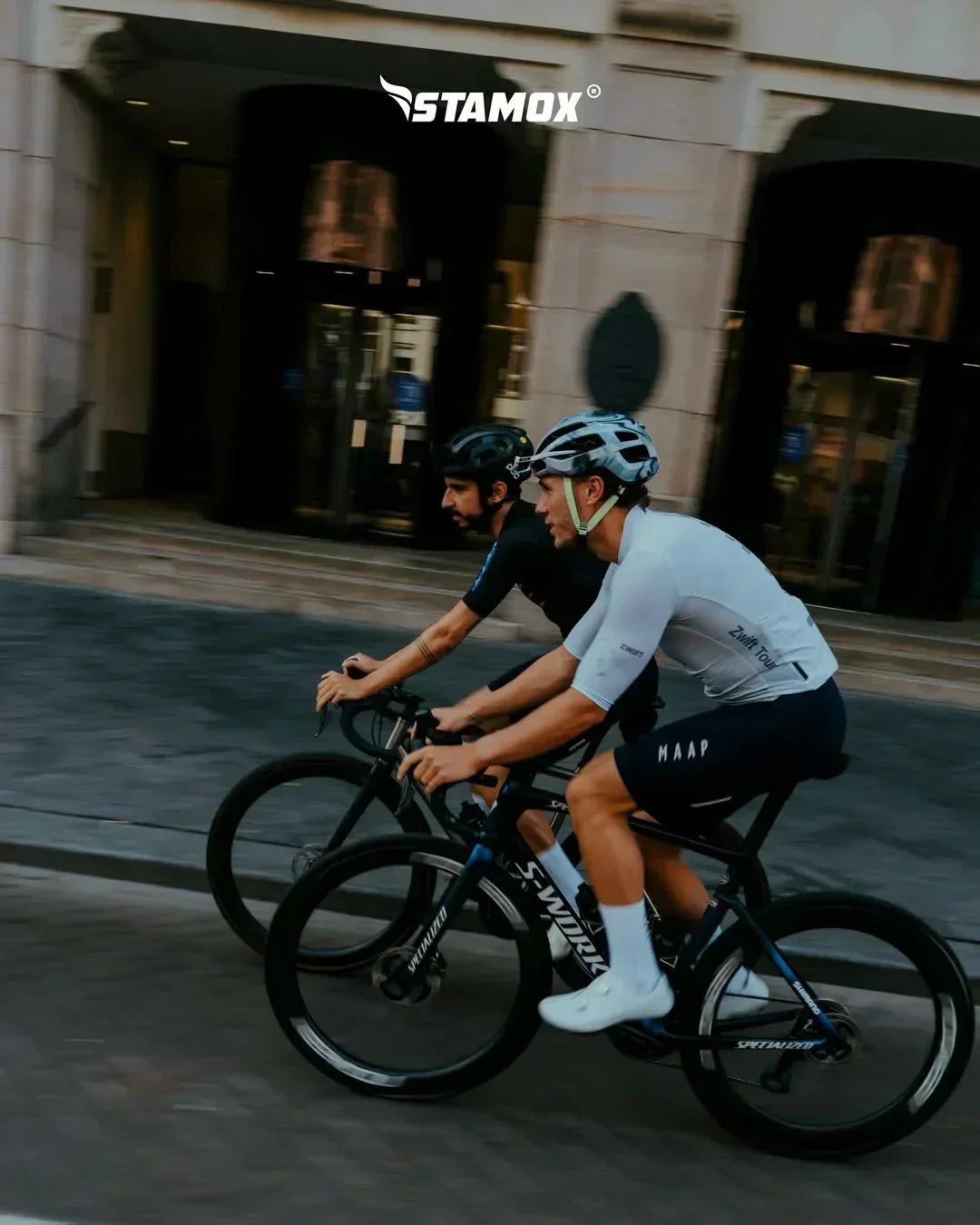Two cyclists riding road bikes outdoors, promoting stamox beetroot powder for endurance.