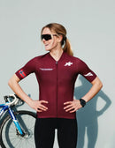 Female cyclist in maroon jersey with Stamox branding, bike in background, Stamox Beetroot Powder