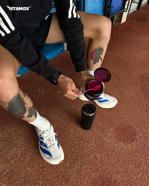 Athlete scooping stamox beetroot powder into a shaker on a track, fitness supplement