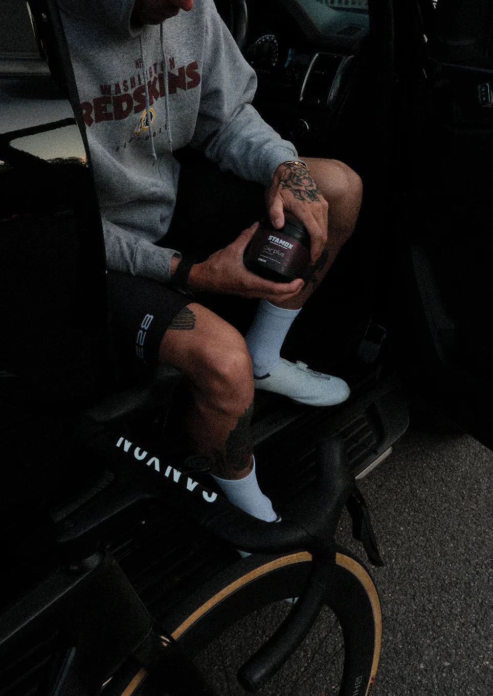 Cyclist holding Stamox beetroot powder jar beside Canyon bike, promoting endurance supplement.