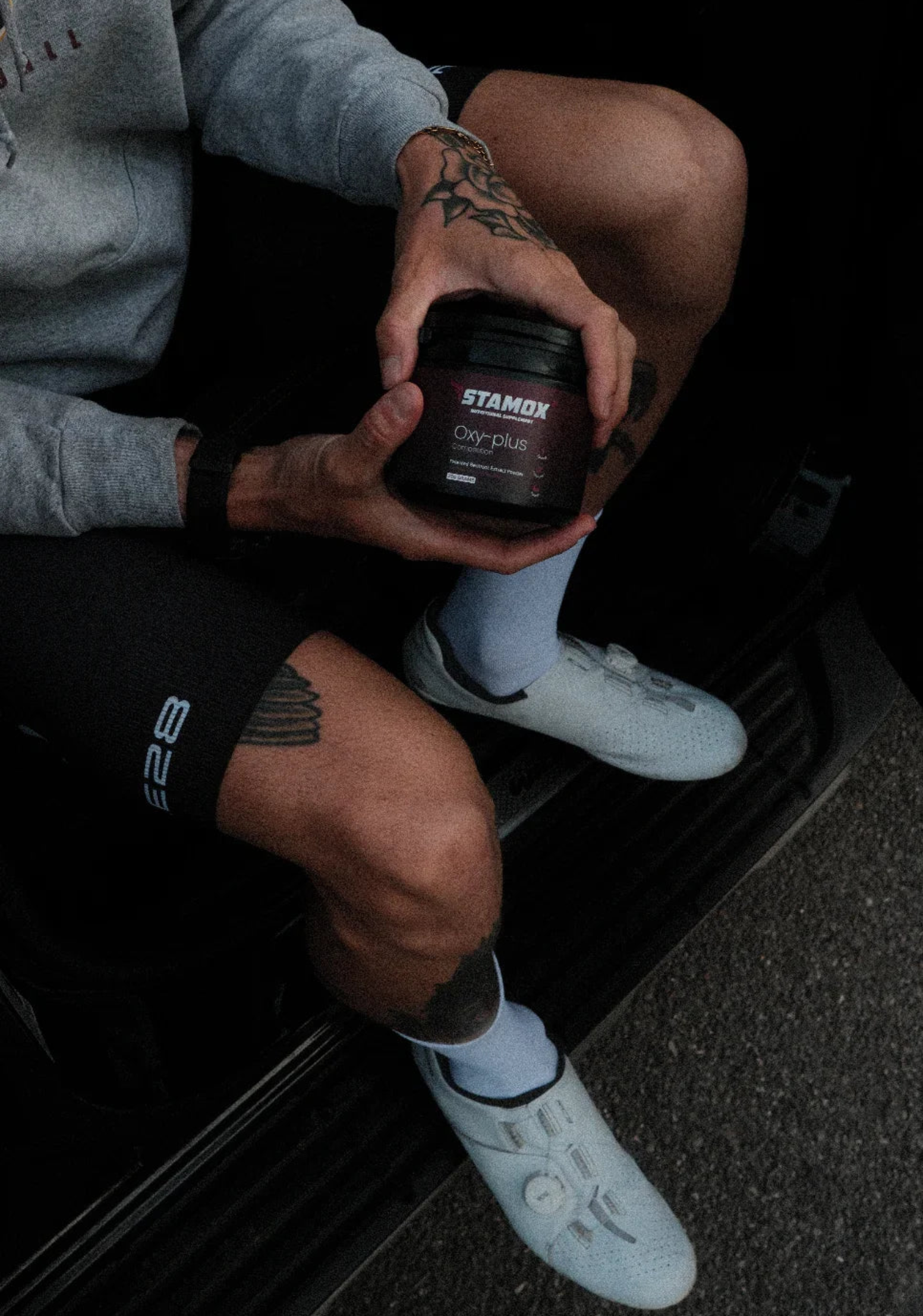 Athlete holding stamox beetroot powder jar, wearing cycling gear and white shoes