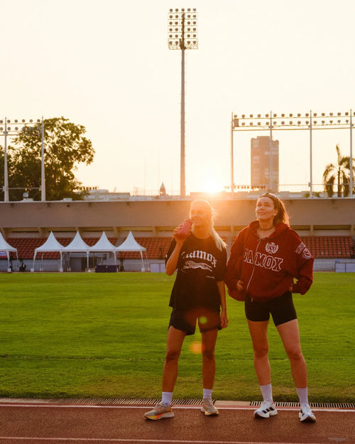 Two women athletes on a track field at sunset with stamox beetroot powder drink