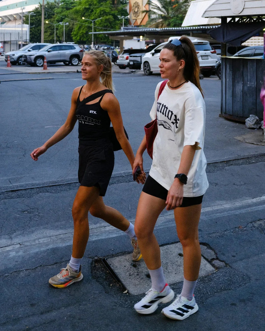 Two women in sporty outfits walking outdoors, wearing shirts with stamox beetroot powder branding