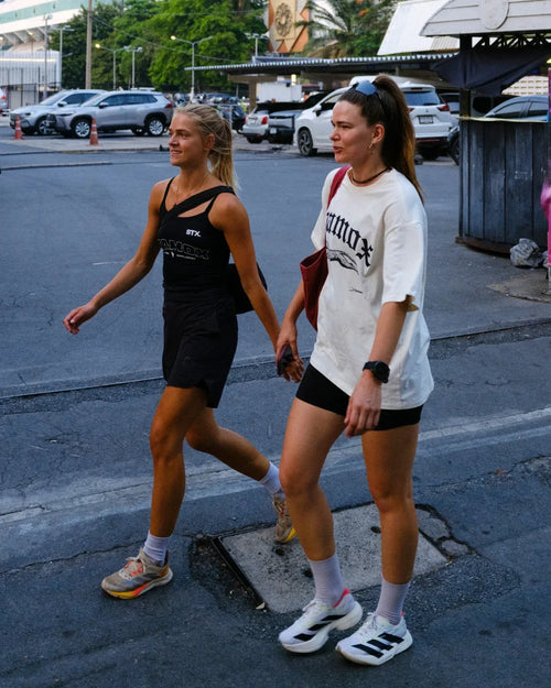 Two women in sporty outfits walking outdoors, wearing shirts with stamox beetroot powder branding