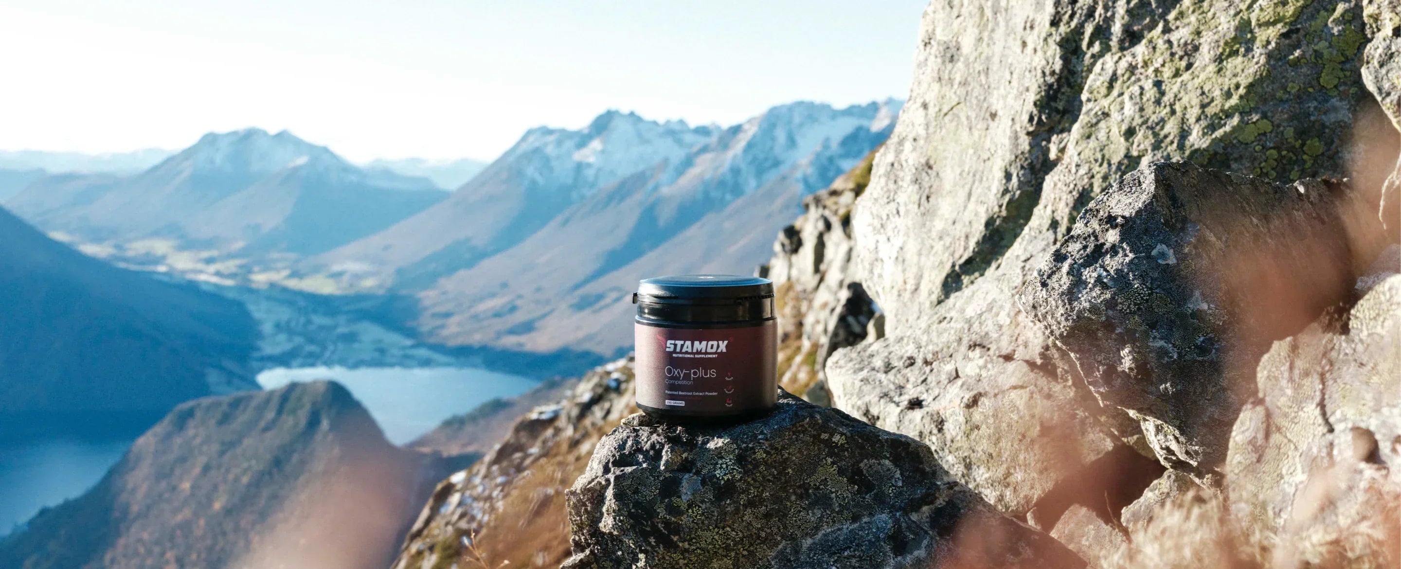 Stamox beetroot powder container on mountain rock with scenic snowy peaks in background