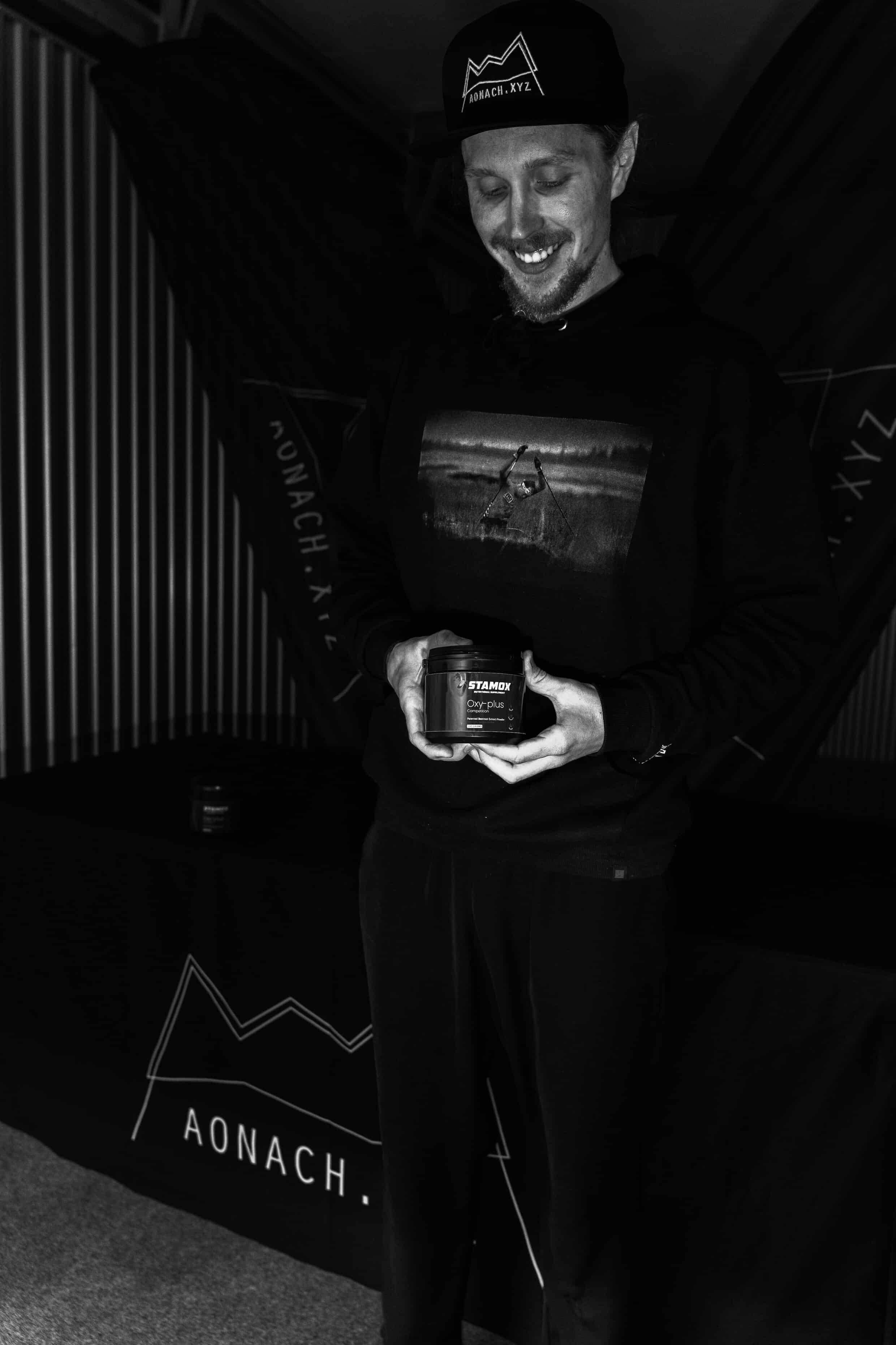 Man smiling and holding Stamox beetroot powder container in a dark indoor setting