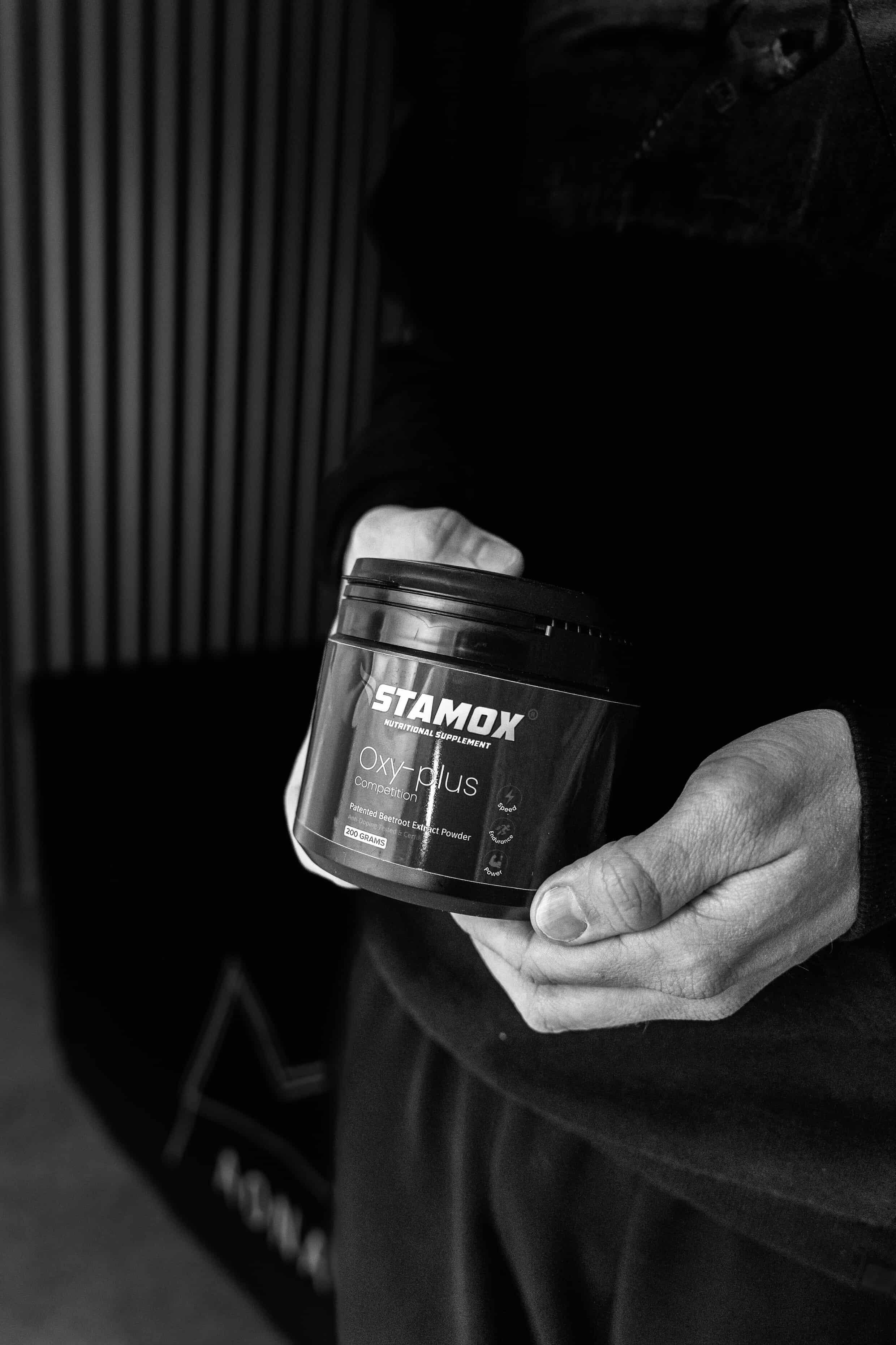 Person holding Stamox beetroot powder supplement container, black and white setting