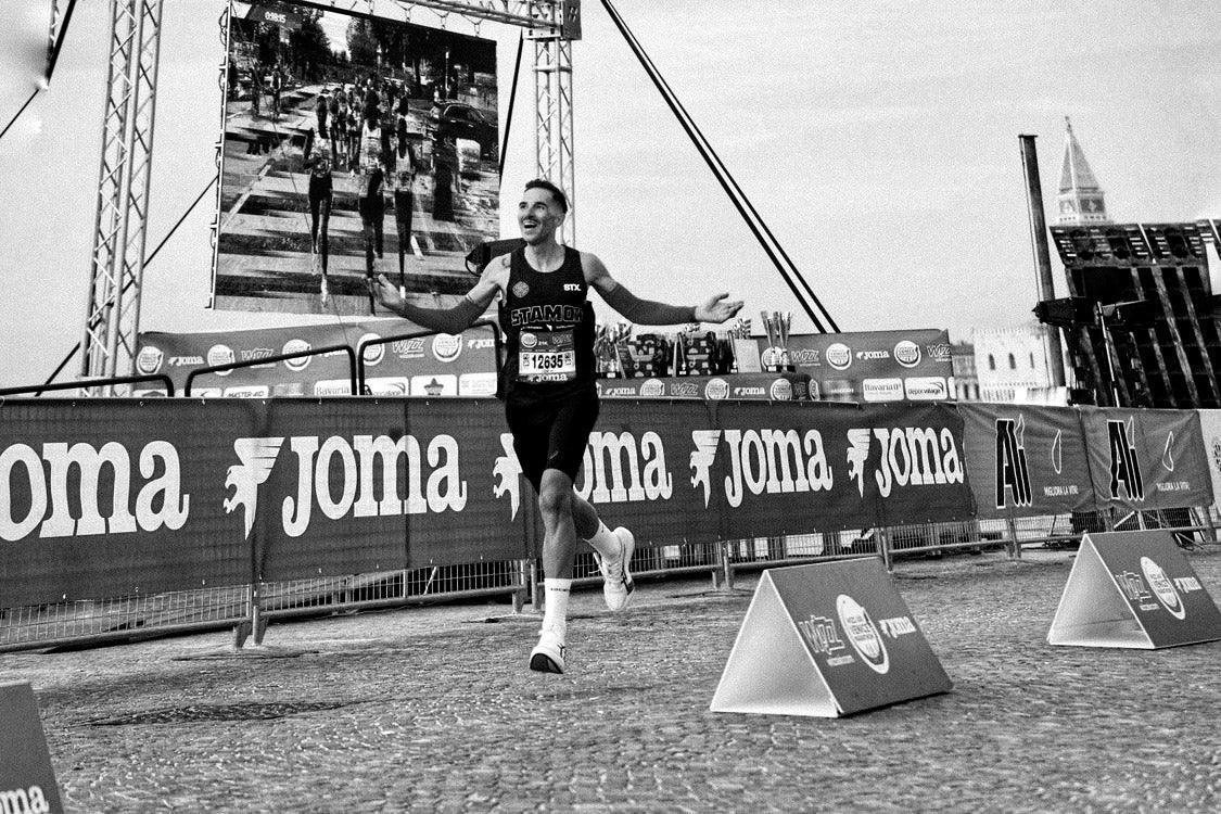 Runner finishing race in athletic gear with stamox beetroot powder logo, outdoor event