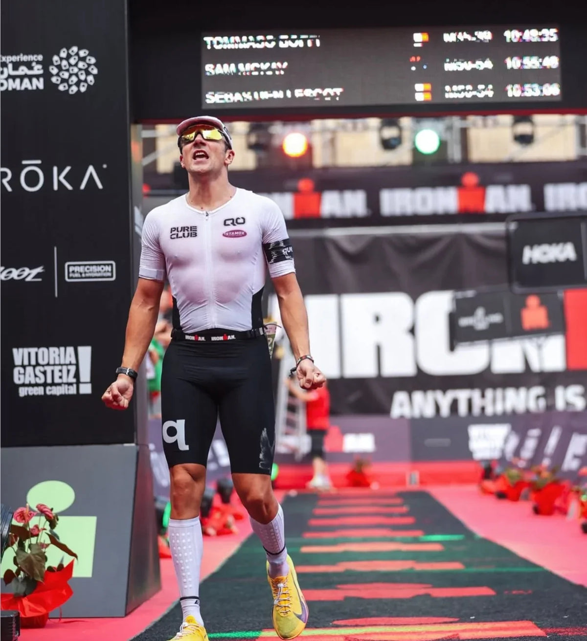 Athlete celebrating at IRONMAN finish line, wearing performance gear and yellow shoes
