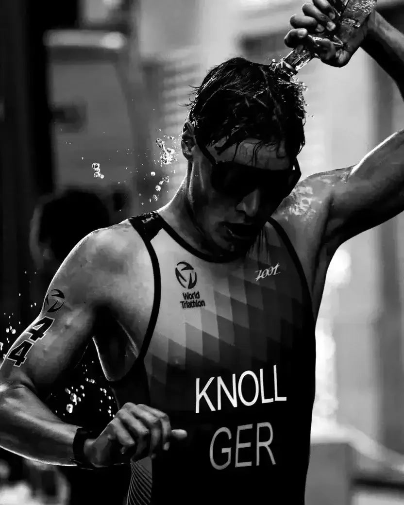 Athlete splashing water on his head during a race, wearing a tank top with 'Knoll GER' branding.