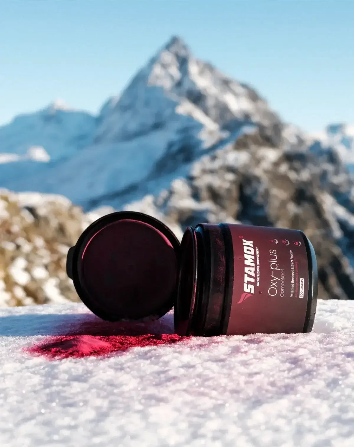 Stamox beetroot powder container open on snowy mountain with red powder spilled