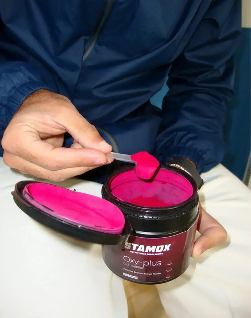 Hand scooping bright red stamox beetroot powder from open supplement container