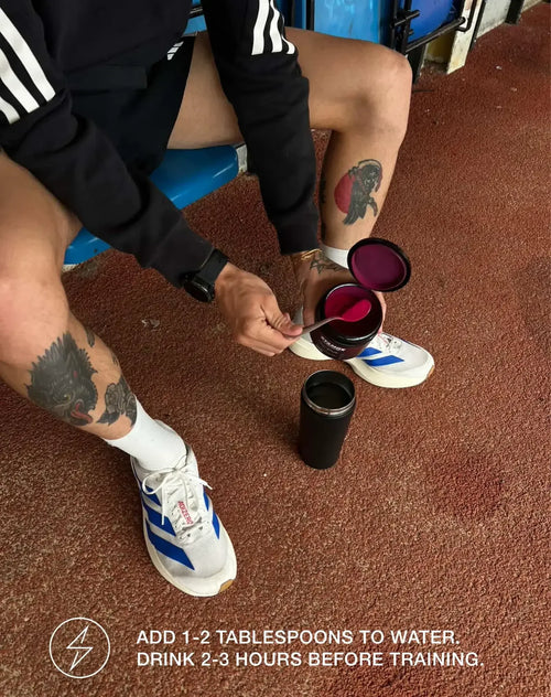 Athlete scooping stamox beetroot powder into a shaker bottle before workout on running track.