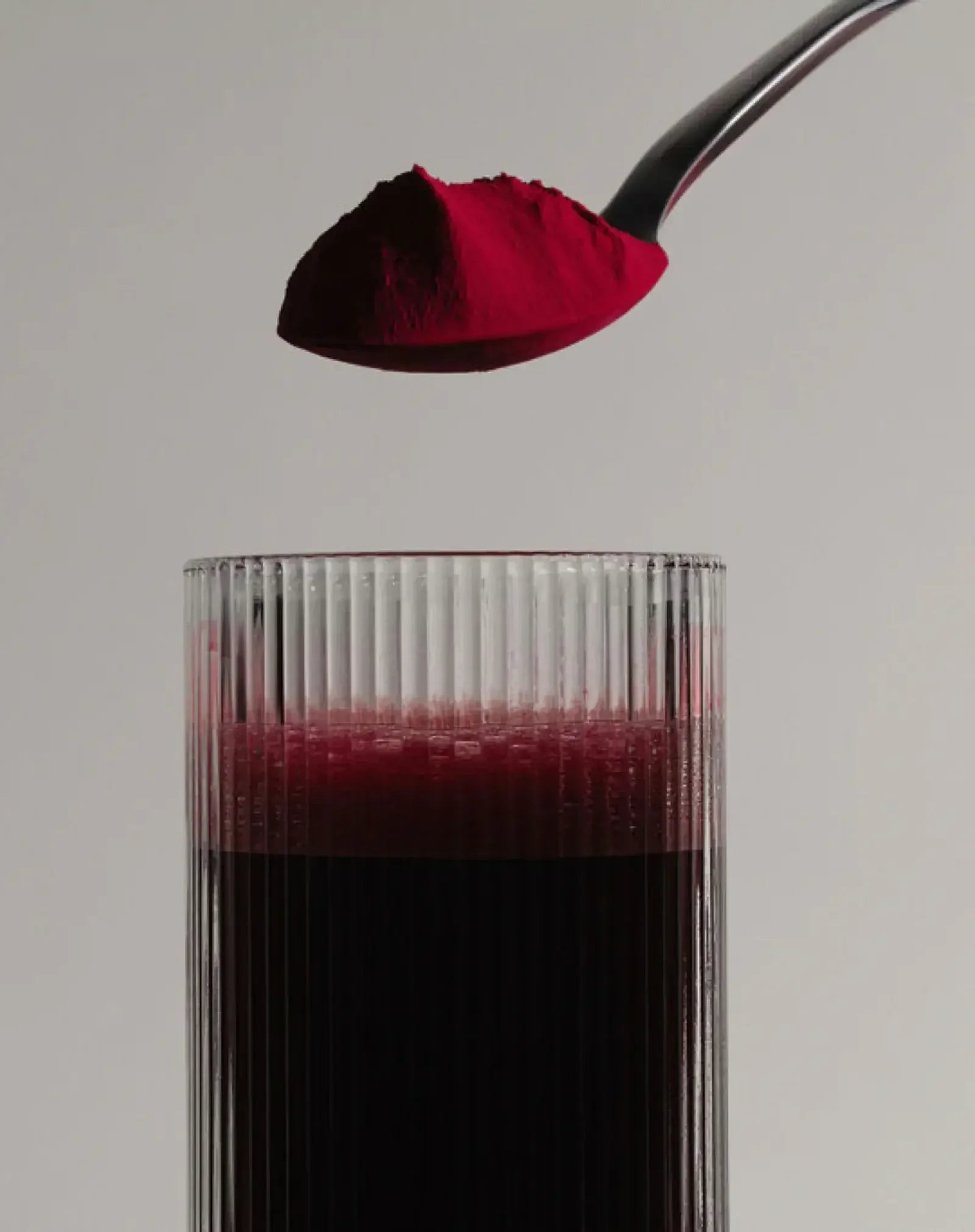 Spoonful of stamox beetroot powder above a glass of dark red beet juice