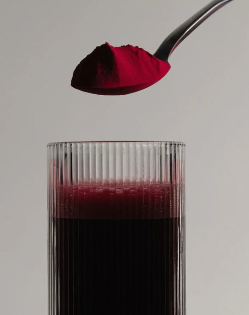 Spoonful of stamox beetroot powder above a glass of dark red beet juice