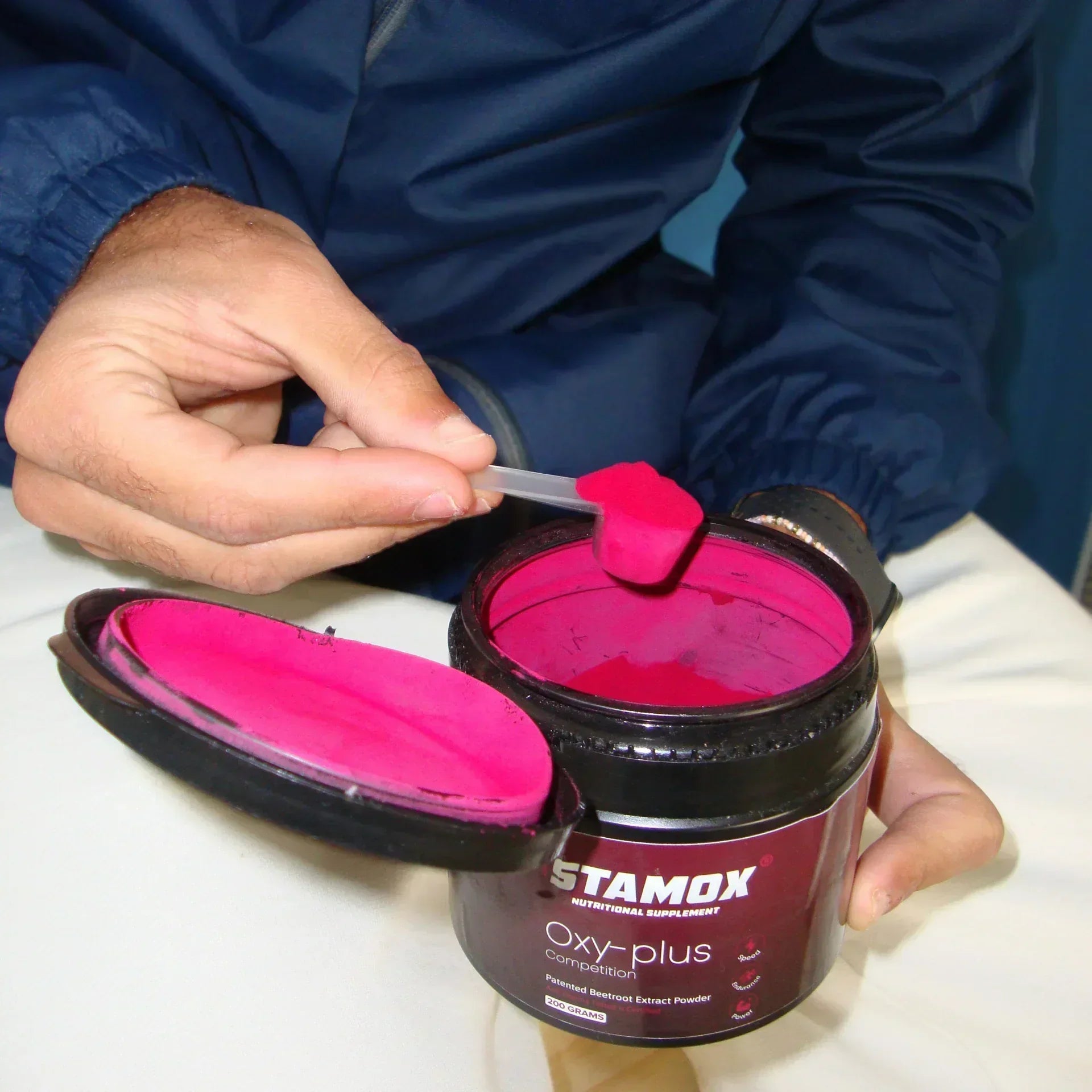 Hand scooping Stamox beetroot powder from open container, bright pink supplement.