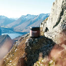 Stamox beetroot powder container on rocky mountain ledge with distant snow-capped peaks and lake