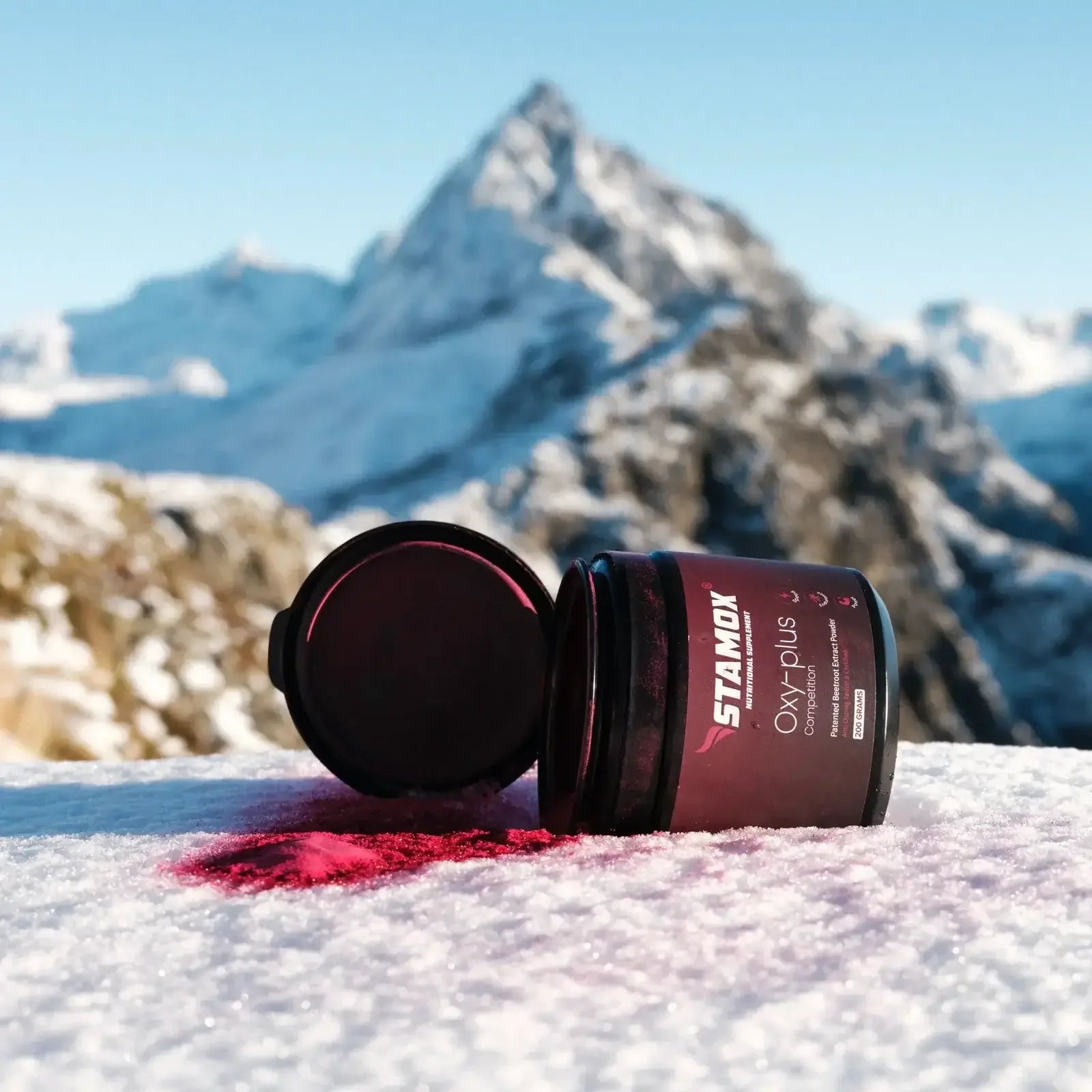 Stamox beetroot powder container on snowy mountain with powder spilled on snow