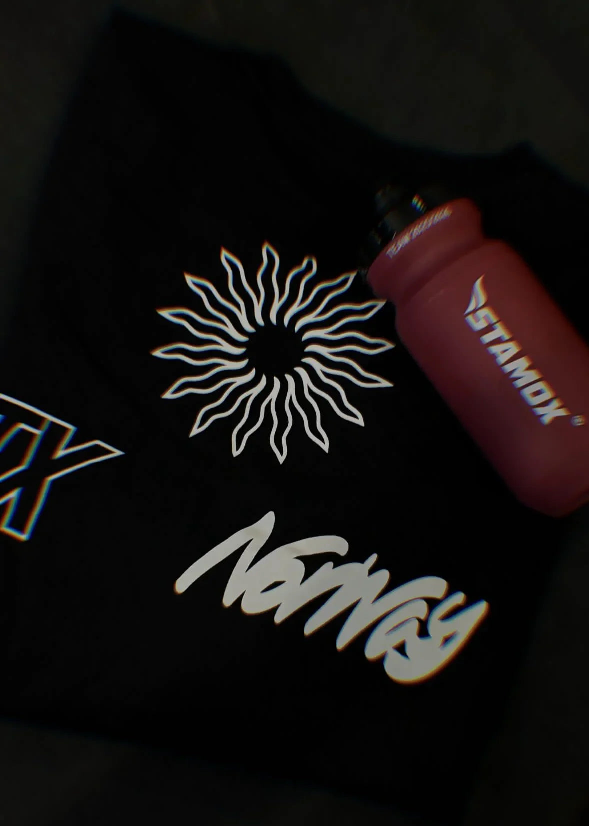 Black shirt with white embroidered designs and a red marker on a dark background. stamox oversized black t shirt and drink bottle