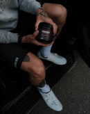 Athlete sitting with stamox beetroot powder container, wearing cycling gear and white shoes