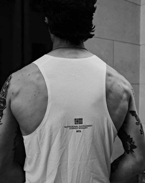 Man with tattoos wearing a white athletic tank top promoting stamox beetroot powder.